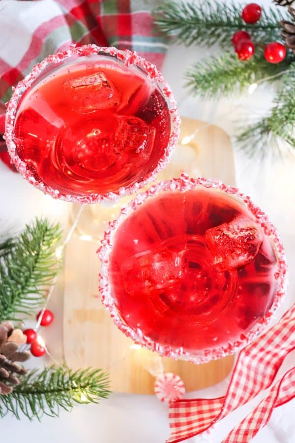 Two red drinks in cocktail glasses with candy cane garnish and ice.