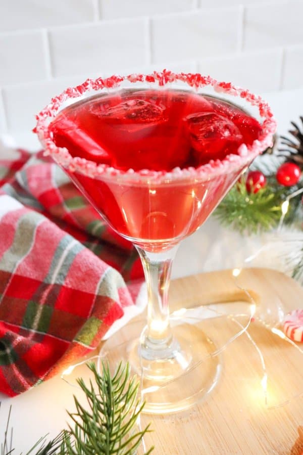 Red drink in a cocktail glass with candy cane garnish and ice.