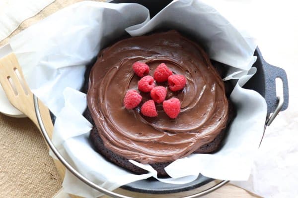 Chocolate Cake with chocolate frosting topped with fresh raspberries in a parchment paper lined cast iron dutch oven.