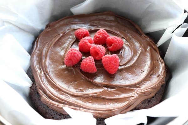 Chocolate Cake with chocolate frosting topped with fresh raspberries in a parchment paper lined cast iron dutch oven.