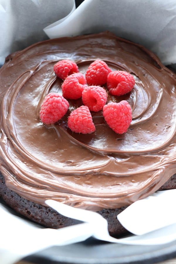 Chocolate Cake with chocolate frosting topped with fresh raspberries in a parchment paper lined cast iron dutch oven.