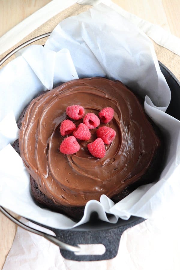 Chocolate Cake with chocolate frosting topped with fresh raspberries in a parchment paper lined cast iron dutch oven.