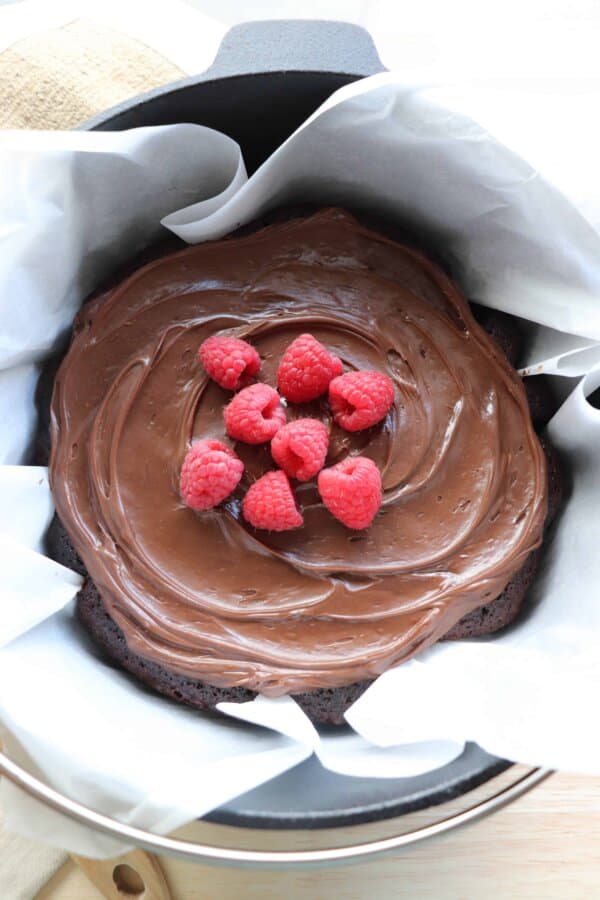Chocolate Cake with chocolate frosting topped with fresh raspberries in a parchment paper lined cast iron dutch oven.