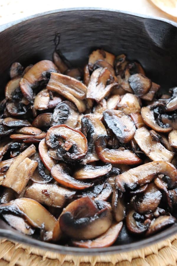 Close up of sliced white mushrooms fried in a cast iron skillet.