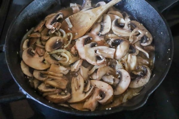 Sliced white mushrooms fried in a cast iron skillet.