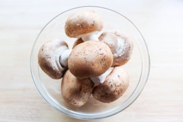 skillet philly cheesesteak recipe Raw mushrooms in a clear bowl on a wood table.