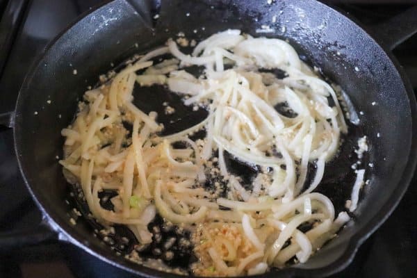 skillet philly cheesesteak recipe Sliced white onion cooking in a cast iron skillet.