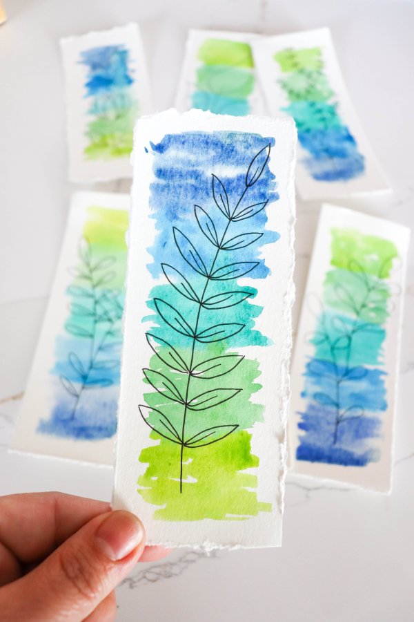 A blue and green watercolor bookmark with a drawing of leaves on a stem.