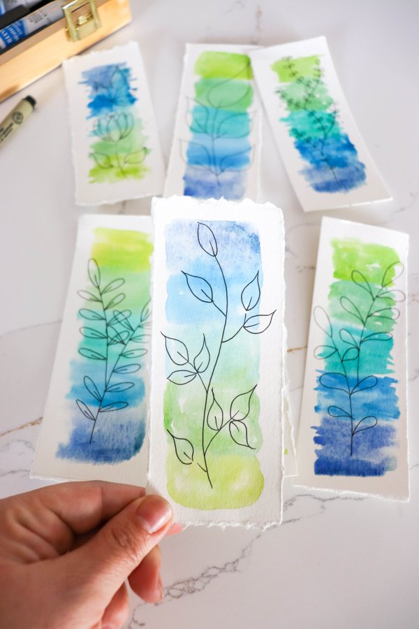 A blue and green watercolor bookmark with a drawing of leaves on a stem.