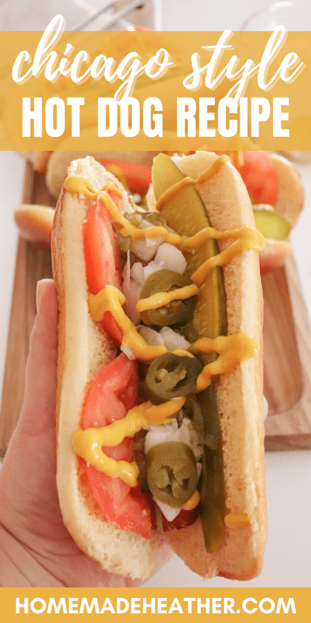 Hot dog topped with pickle spears, sliced tomatoes, diced onion, pickled peppers and mustard held in a hand.