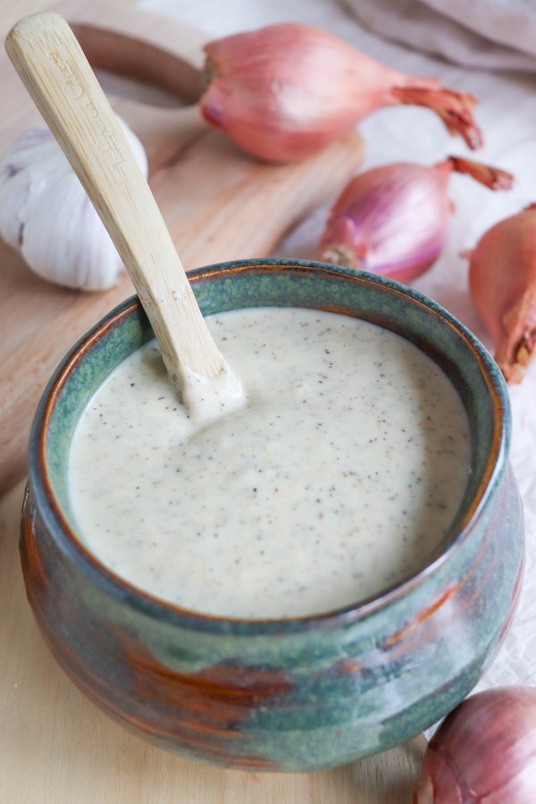 White Sauce with black pepper flakes in a blue dish with a wooden spoon handle coming out.