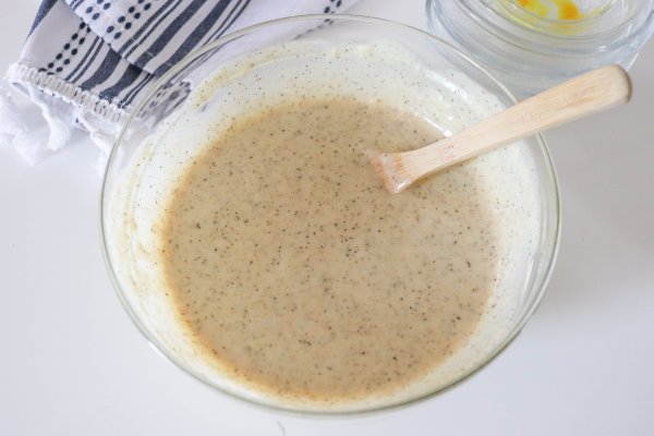 Alabama white sauce in a clear class bowl with a wooden spoon handle coming out on a white counter.