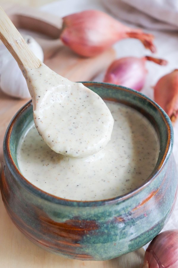 Alabama White Sauce with black pepper flakes in a blue dish with a wooden spoon.
