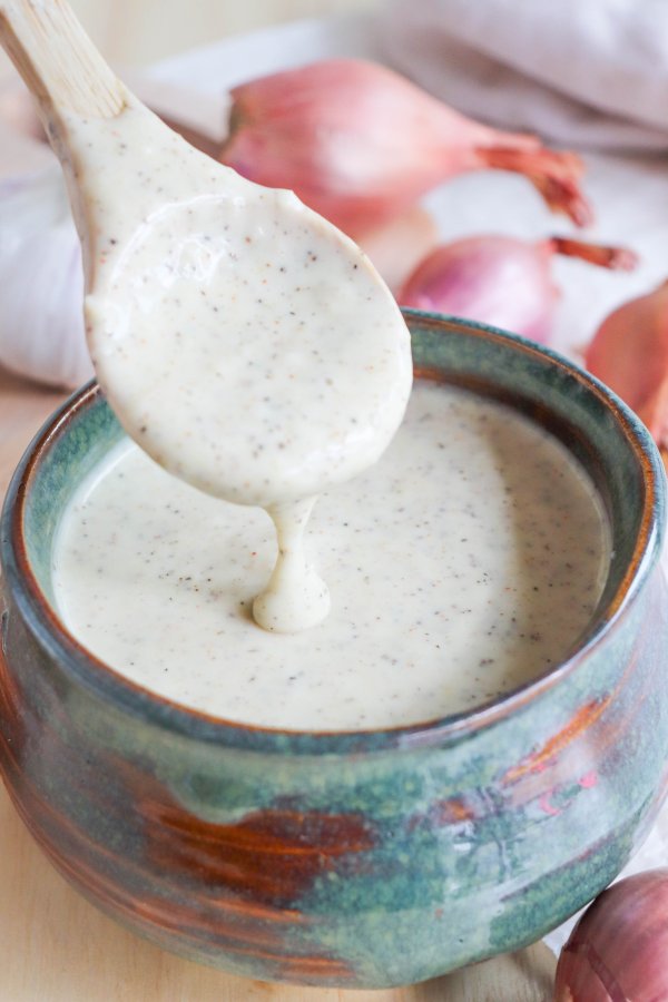 Alabama White Sauce with black pepper flakes in a blue dish with a wooden spoon full of sauce dripping back into bowl.