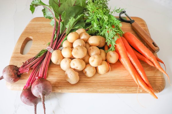 Beets, potatoes and carrots on a wooden cutting board.