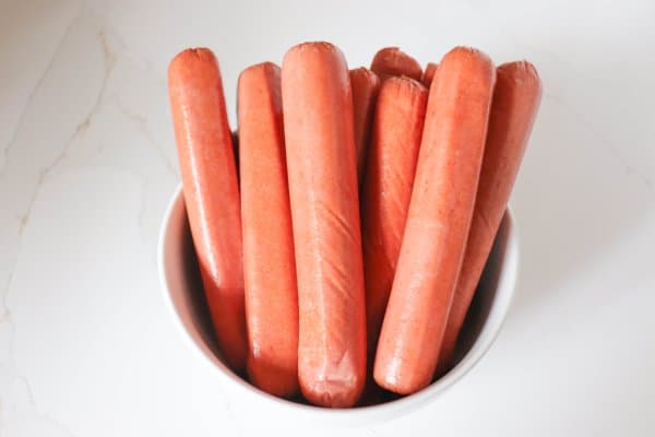 Raw hot dogs in a white bowl.