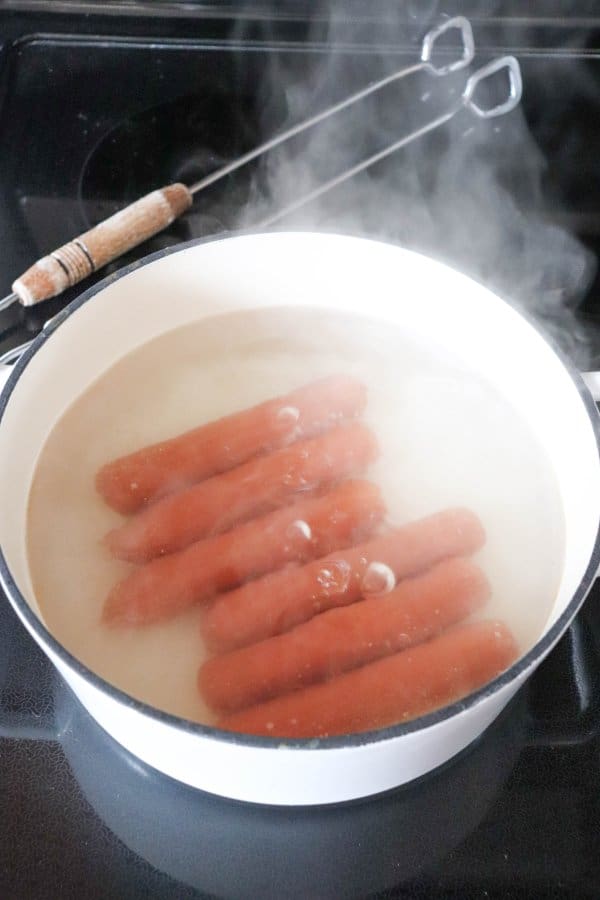White dutch oven full of hot dogs boiling on the stove top.