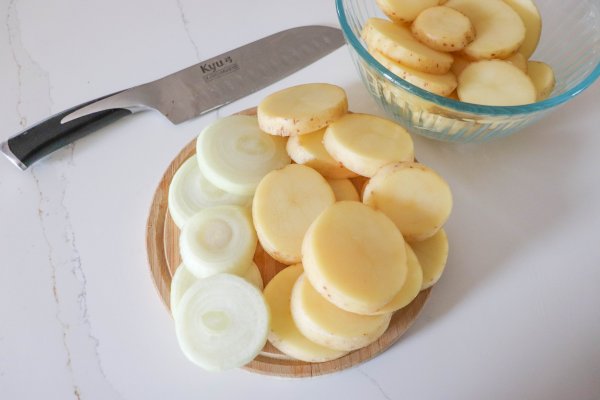 Sliced potatoes and onion on a cutting board.