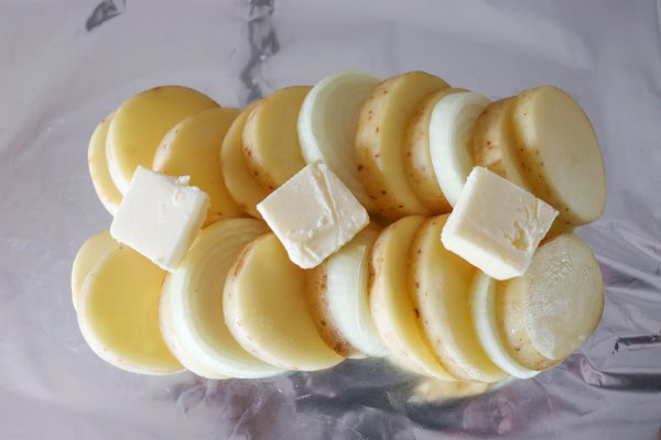 Sliced potatoes and onions layered together and topped with butter on a sheet of foil.