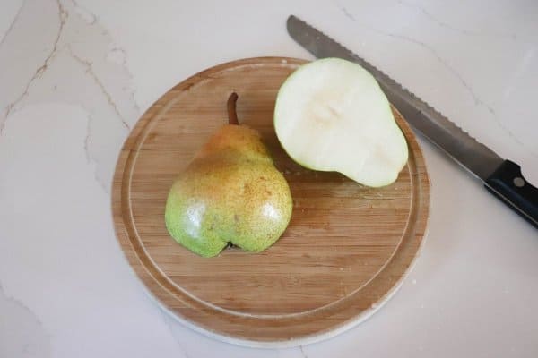 Pear cut in half on a wooden cutting board.