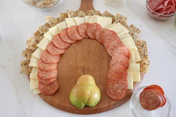 A meat and cheese charcuterie board in the shape of a turkey with a pear body and meat, cheese and cracker feathers.