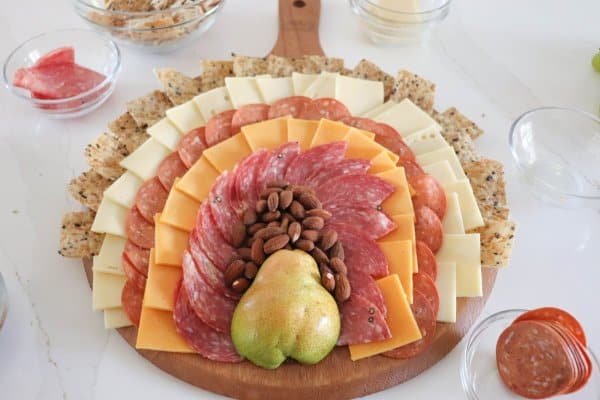 A meat and cheese charcuterie board in the shape of a turkey with a pear body and meat, cheese and cracker feathers.