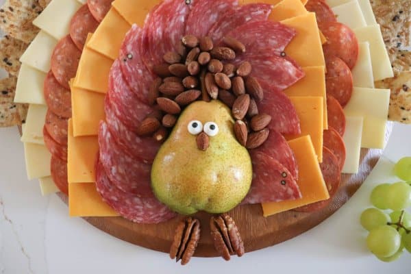 A meat and cheese charcuterie board in the shape of a turkey with a pear body and meat, cheese and cracker feathers.