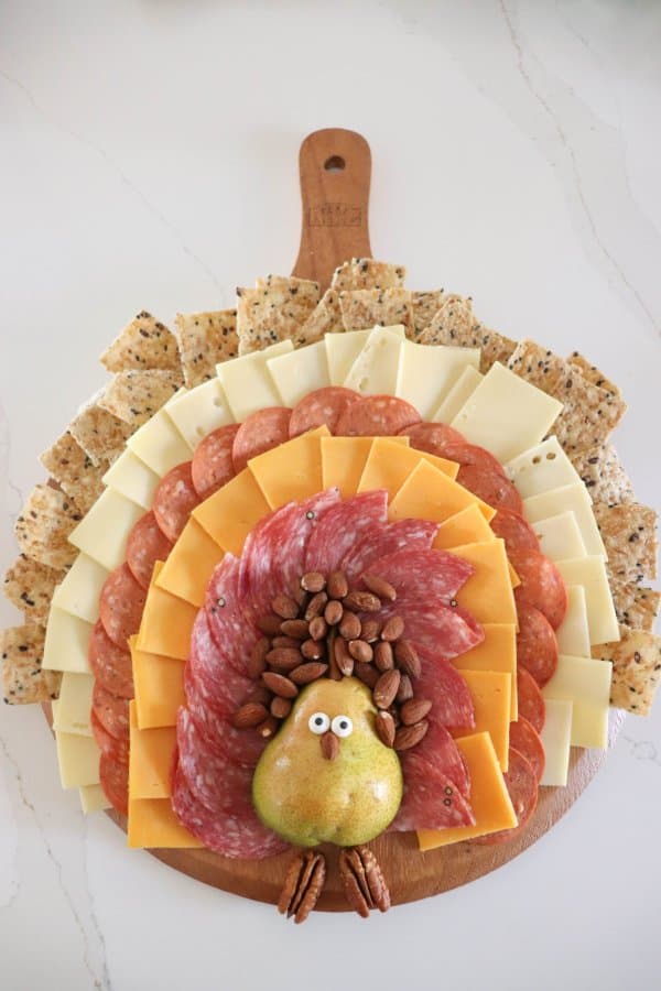 A meat and cheese charcuterie board in the shape of a turkey with a pear body and meat, cheese and cracker feathers.