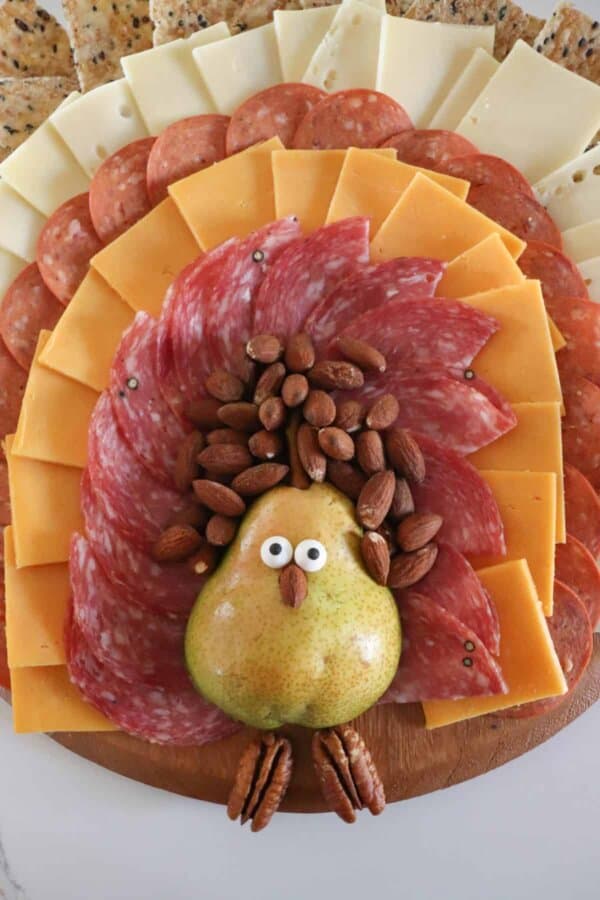A meat and cheese charcuterie board in the shape of a turkey with a pear body and meat, cheese and cracker feathers.