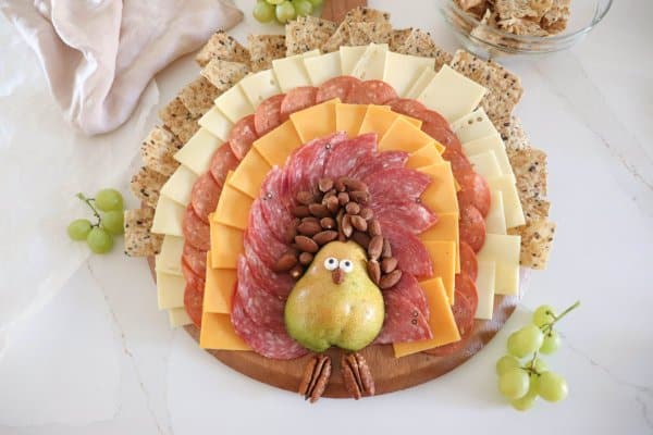 A meat and cheese charcuterie board in the shape of a turkey with a pear body and meat, cheese and cracker feathers.