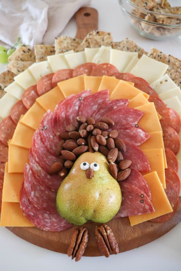 A meat and cheese charcuterie board in the shape of a turkey with a pear body and meat, cheese and cracker feathers.