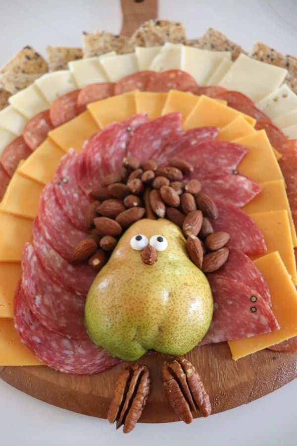 A meat and cheese charcuterie board in the shape of a turkey with a pear body and meat, cheese and cracker feathers.