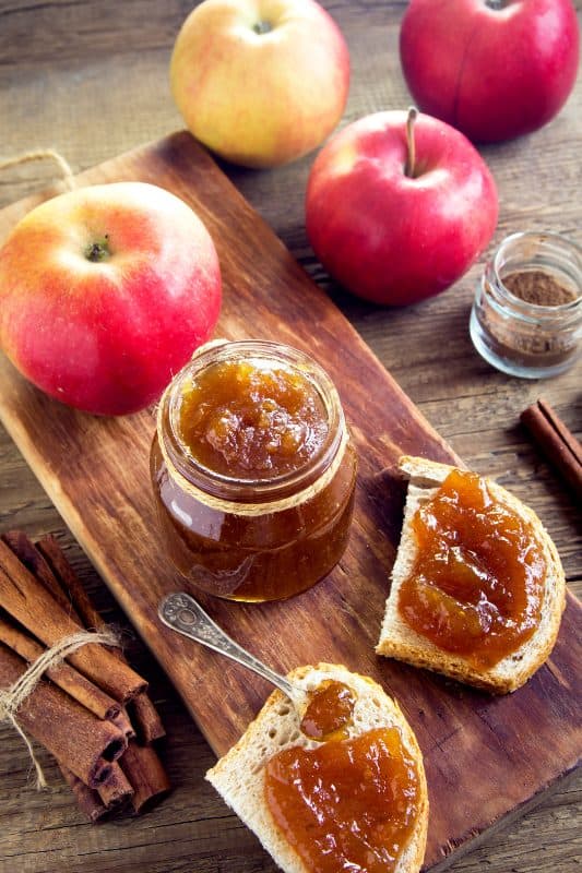 Crockpot apple butter recipe spread on toast, a jar of apple butter, and apples on a wooden surface.