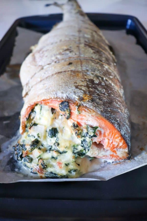 Whole salmon fillet stuffed with crab & spinach cream cheese mixture on parchment paper lined baking sheet.