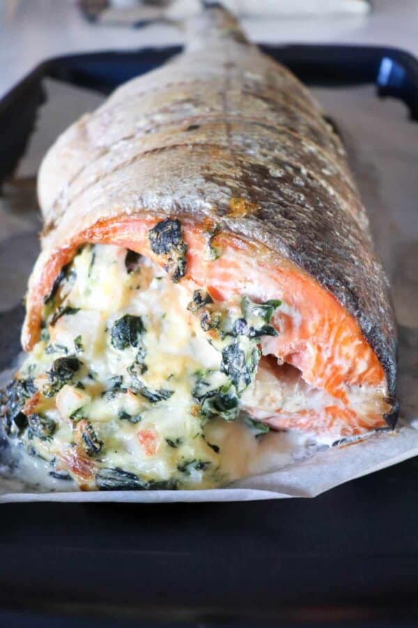 Whole salmon fillet stuffed with crab & spinach cream cheese mixture on parchment paper lined baking sheet.