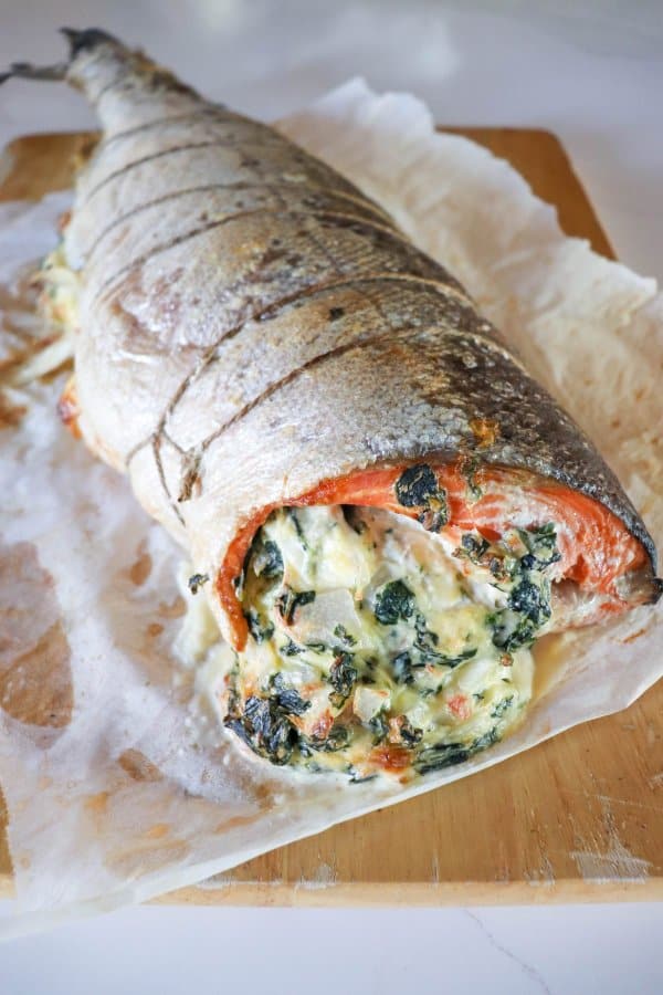 Whole salmon fillet stuffed with crab & spinach cream cheese mixture on parchment paper lined cutting board.