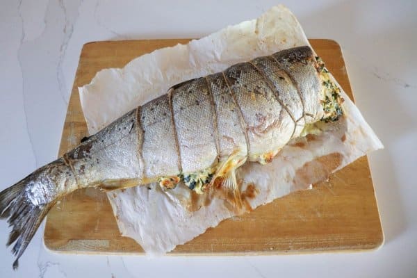 Whole salmon fillet stuffed with crab & spinach cream cheese mixture on parchment paper lined cutting board.