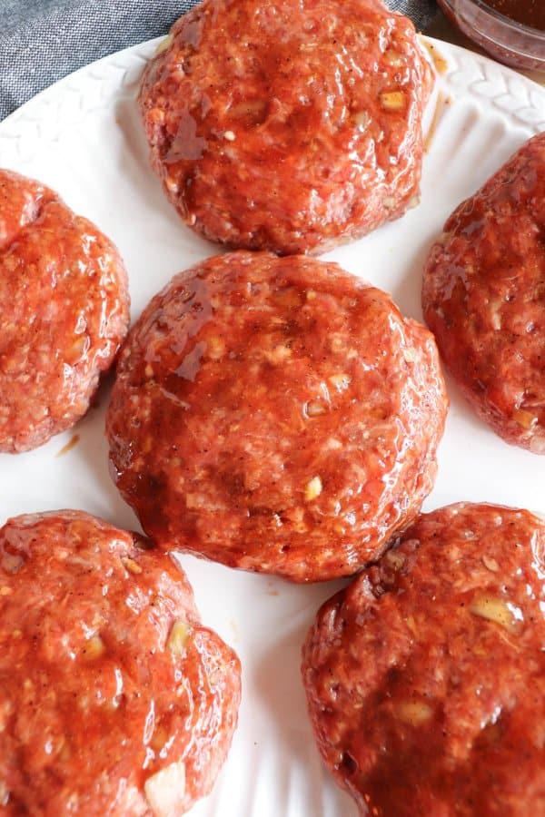 Raw hamburger patties covered in BBQ sauce.