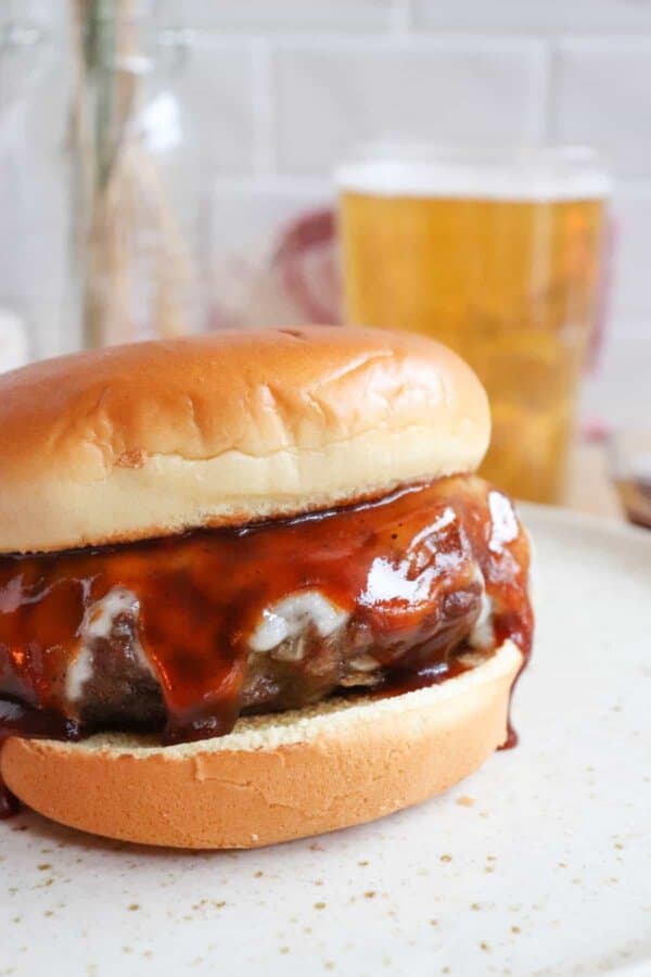 Close up of a hamburger covered in melted cheese and BBQ sauce on a white bun.