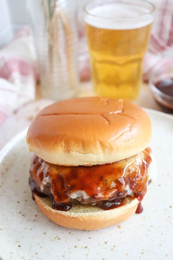 The Best BBQ Hamburger Recipe with a burger on a white bun with melted cheese and barbecue sauce.