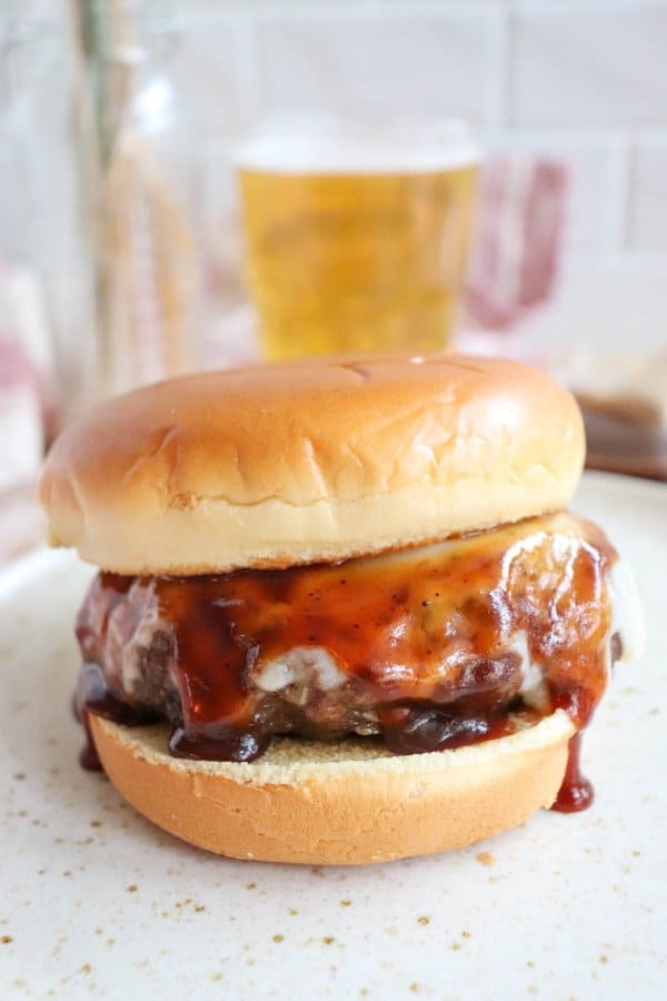 The Best BBQ Hamburger Recipe with a burger on a white bun with melted cheese and barbecue sauce.