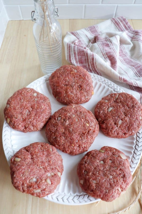 Six homemade hamburger patties on a white plate.