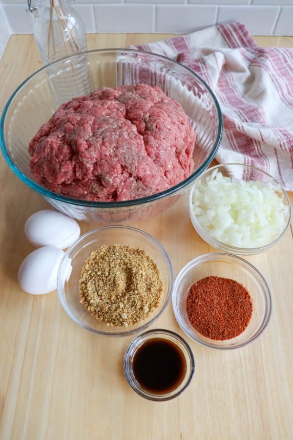 Hamburger Pattie Ingredients in clear glass bowls on a wooden table.