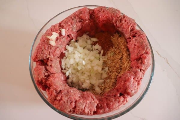 Raw ground beef in a bowl with diced onion and spices.
