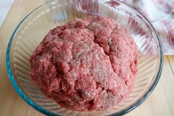 Raw ground beef in a large clear glass mixing bowl.