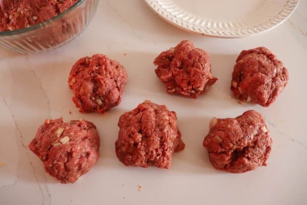 Raw hamburger patties rolled into six balls on a white counter.