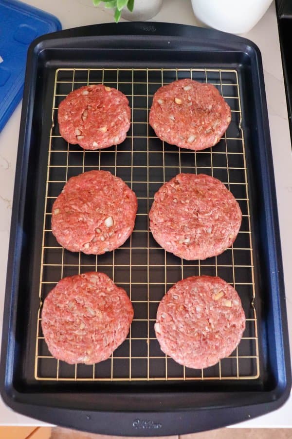 Six raw hamburger patties on a wire rack on a baking sheet.