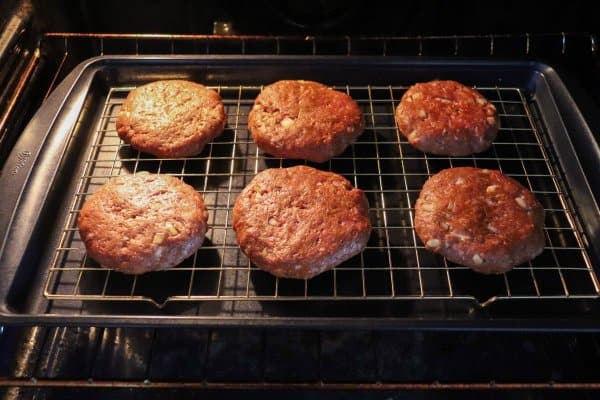 Six raw hamburger patties on a wire rack on a baking sheet in the oven.