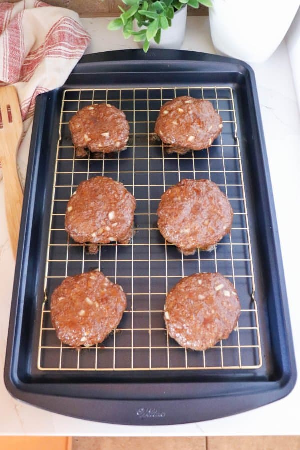 Six cooked hamburger patties on a wire rack on a baking sheet.