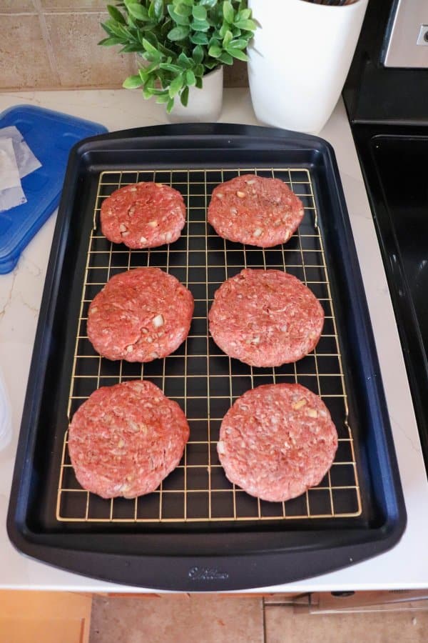 Six raw hamburger patties on a wire rack on a baking sheet.